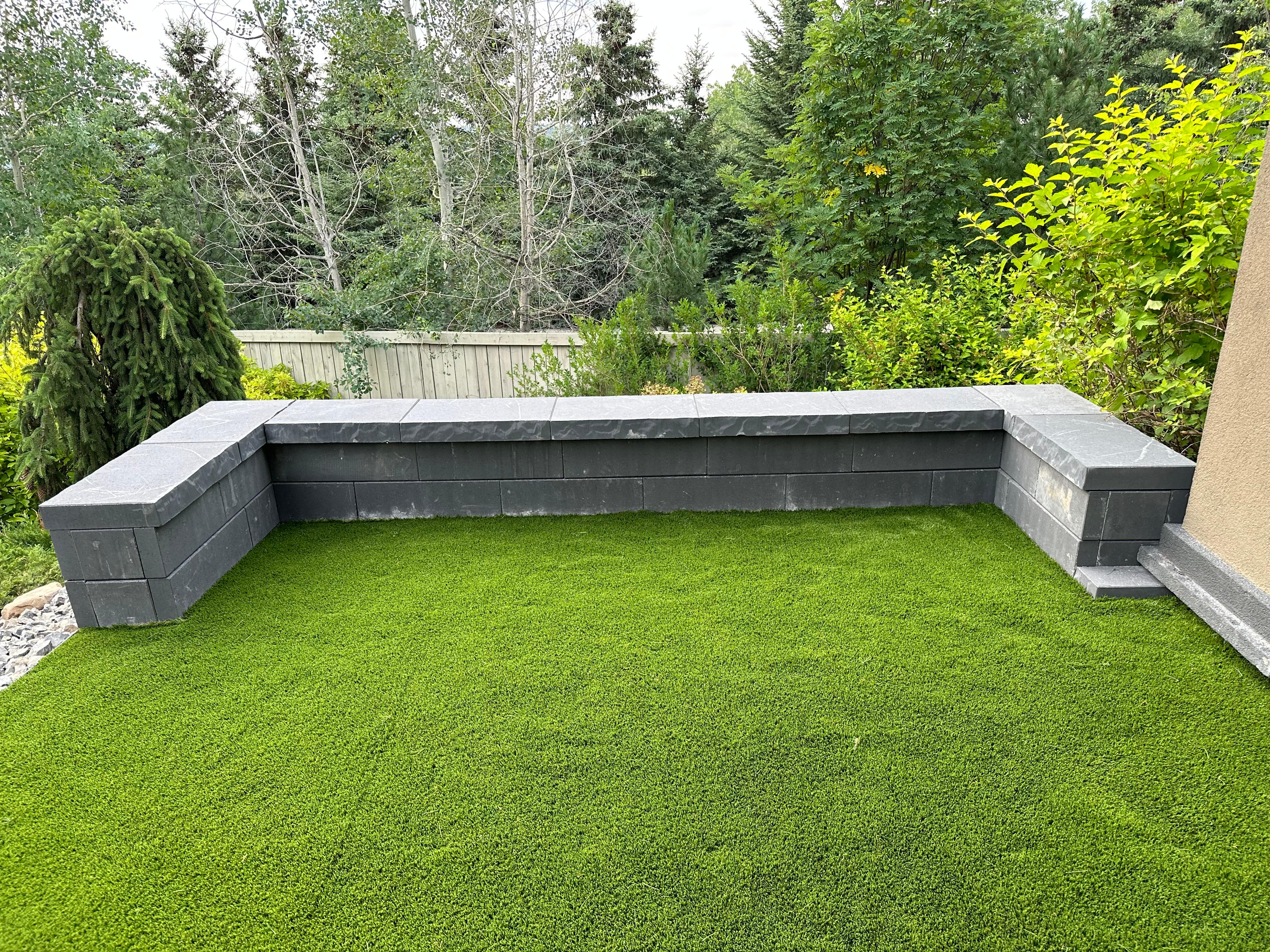 Artificial turf backyard with dark stone retaining wall seating ledge